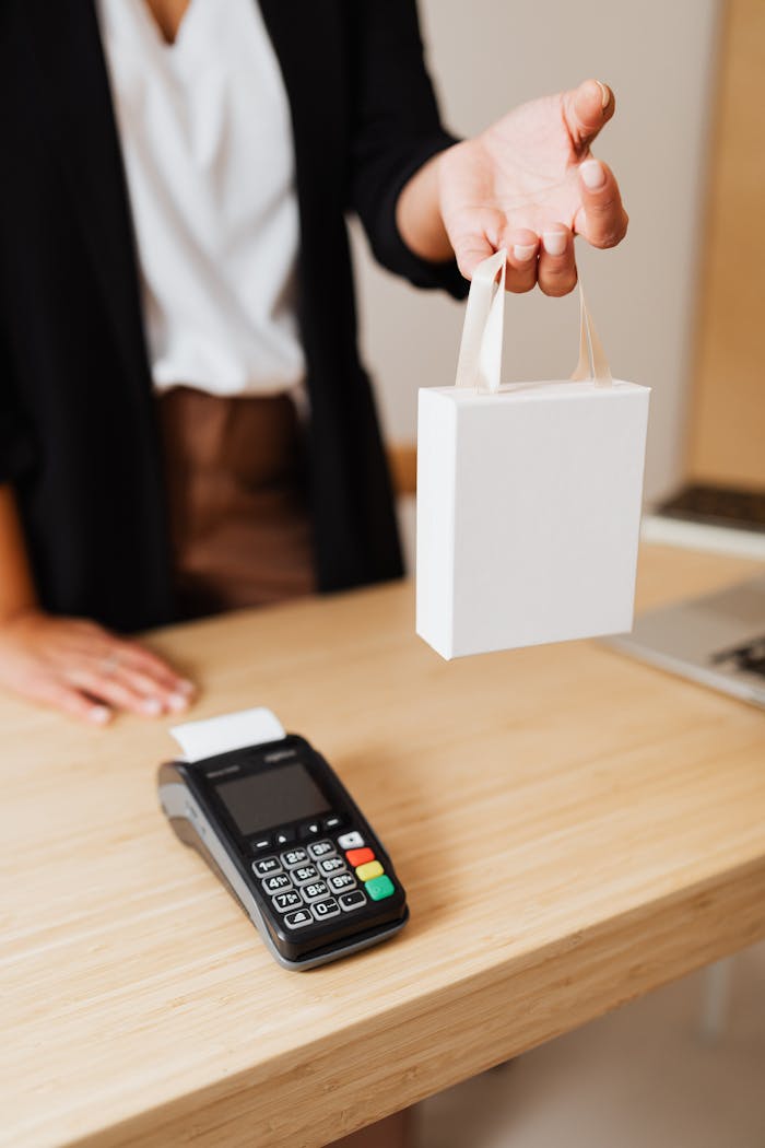 The Art of Drawing Readers In: Your attractive post title goes here Close-up of shopper's hand holding a bag next to a payment terminal on a wooden counter.